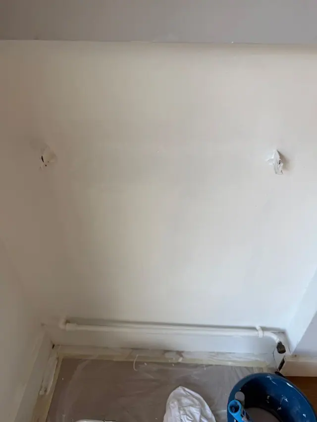 Salon après : mur repeint en blanc derrière l'emplacement du radiateur, pattes de fixation en place.