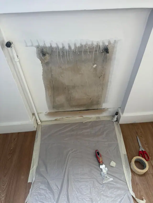Chambre avant : mur gratté derrière le radiateur, traces noires et coulures, sol protégé par une bâche.